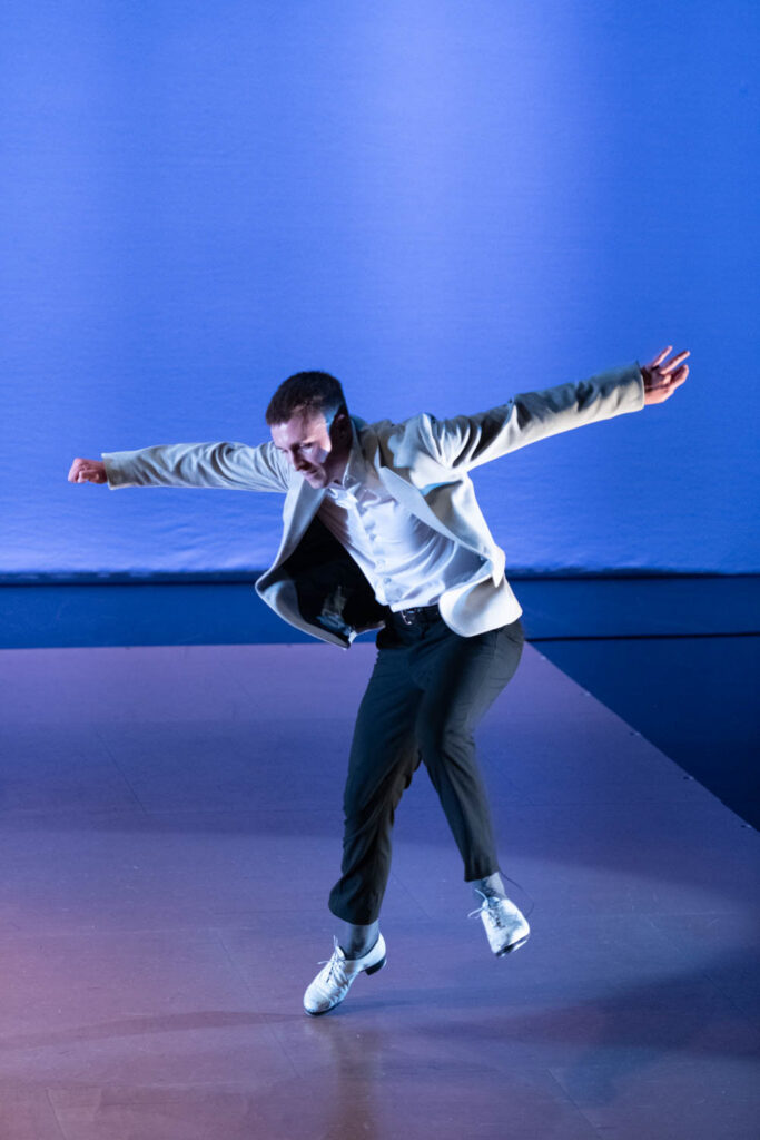 Luke Hickey performs tap dance against a blue lighted backdrop.